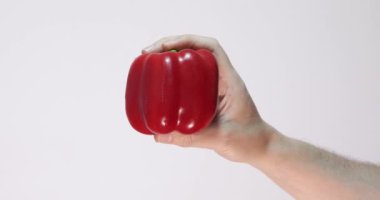 Kırmızı biber ön planda beyaz arka planda bir elle tutulur.