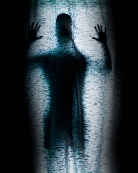 Silhouette of man behind sheet or shroud surrounded by darkness.