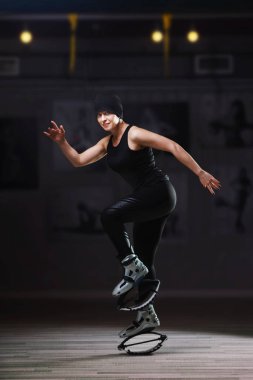 Siyah spor kıyafetli gülümseyen kadın zıplayan ayakkabıyla zıplıyor.