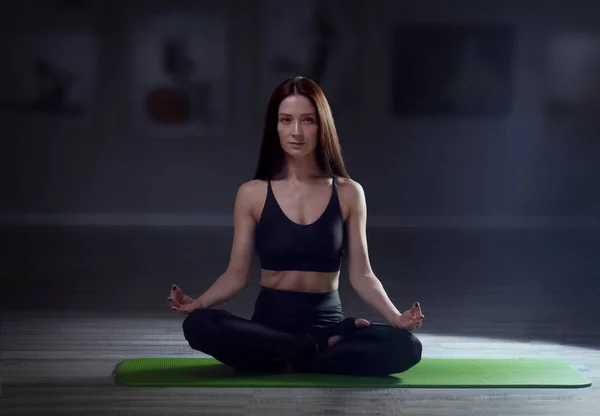 Jeune femme en bonne santé pratiquant le yoga et assis dans le padmasana à la salle d'entraînement — Photo