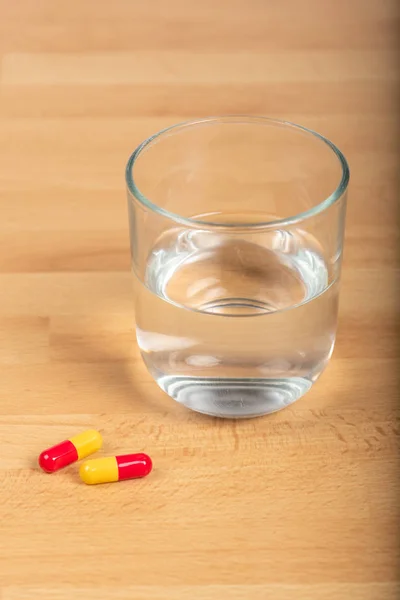 Capsule di paracetamolo e bicchiere d'acqua su un tavolo di legno — Foto Stock