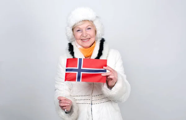 持有挪威国旗的高级妇女 成年妇女70岁 老女人穿着暖和的冬衣站在浅色的背景 — 图库照片