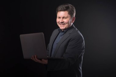 İş adamı koyu arka plan üzerinde elinde bir dizüstü bilgisayar ile orta yaşlı.