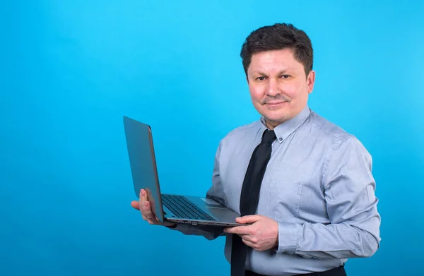 中年商人手持笔记本电脑在蓝色背景 文本位置 — 图库照片