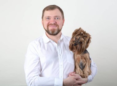 Sakallı adam kollarını gri arka plan üzerinde bir küçük Yorkshire terrier köpek tutar.