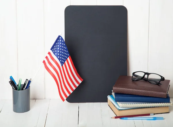 Books, notebooks, a note board and the US flag on a wooden table. English language learning. Education in United States of America.
