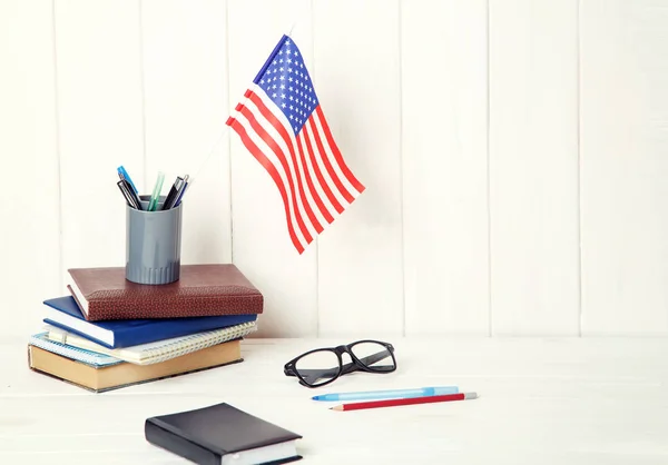 Books, exercise books, glasses and the US flag on a wooden table. English language learning. Education in United States of America.