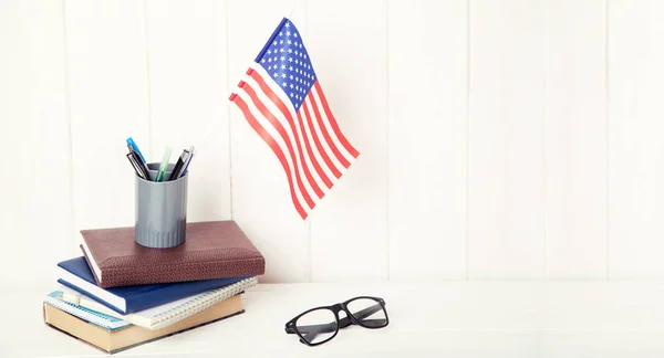 Books, exercise books, glasses and the US flag on a wooden table. English language learning. Education in United States of America.