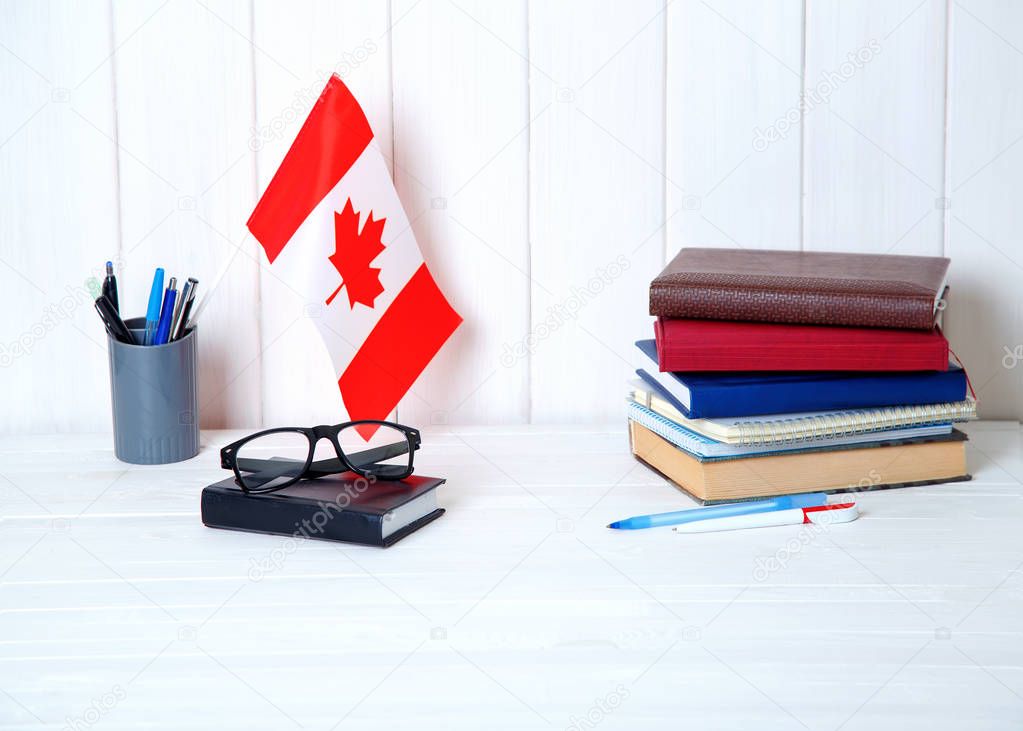 Books, notebooks, textbooks, glasses, a flag on a wooden table. Education in Canada, North America.
