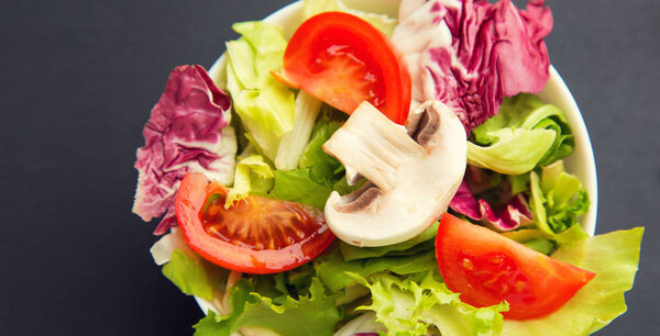 Close-up of a salad mix of fresh green leaves frieze, radicchio, endive, tomato and mushroom champignon on a gray table. Dietary vegetable menu.