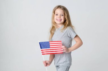 Amerika Birleşik Devletleri bayrağı gri bir arka plan üzerinde olan küçük kız. Sarışın kız bir ışık gri gömlek 6 yaşında.