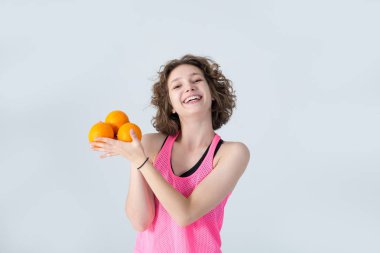 Kıvırcık gülümseyen kadın elinde turunçgil meyveleri ve şeftali tutuyordu. Gri arka planda duruyordu. Pembe formalı mutlu kız diyet egzersizleri yapıyor..