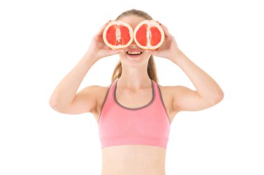 Pembe jimnastik tişörtü giymiş, elinde kesik greyfurt tutan çekici bir genç kadın. Komik kız beyaz arka planda gözlerinde narenciye meyveleri tutuyor..