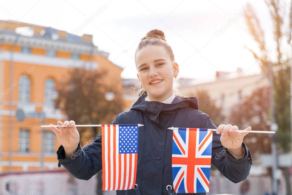 Teenager girl with two US and UK flags on a city street background. Learn English abroad.
