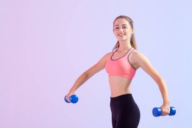 Elinde iki dambıl olan genç bir kadın, mor bir arka plan üzerinde duruyor. Fitness egzersizi.