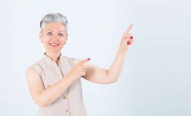 Sağa bak! Orta yaşlı bir kadın, gri bir arka planda durarak, boş alan için parmaklarını kenarı işaret eder..