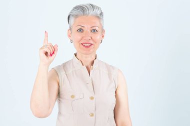 İyi fikir! Orta yaşlı bir kadın parmak kaldırıyor, gri bir arka planda duruyor..