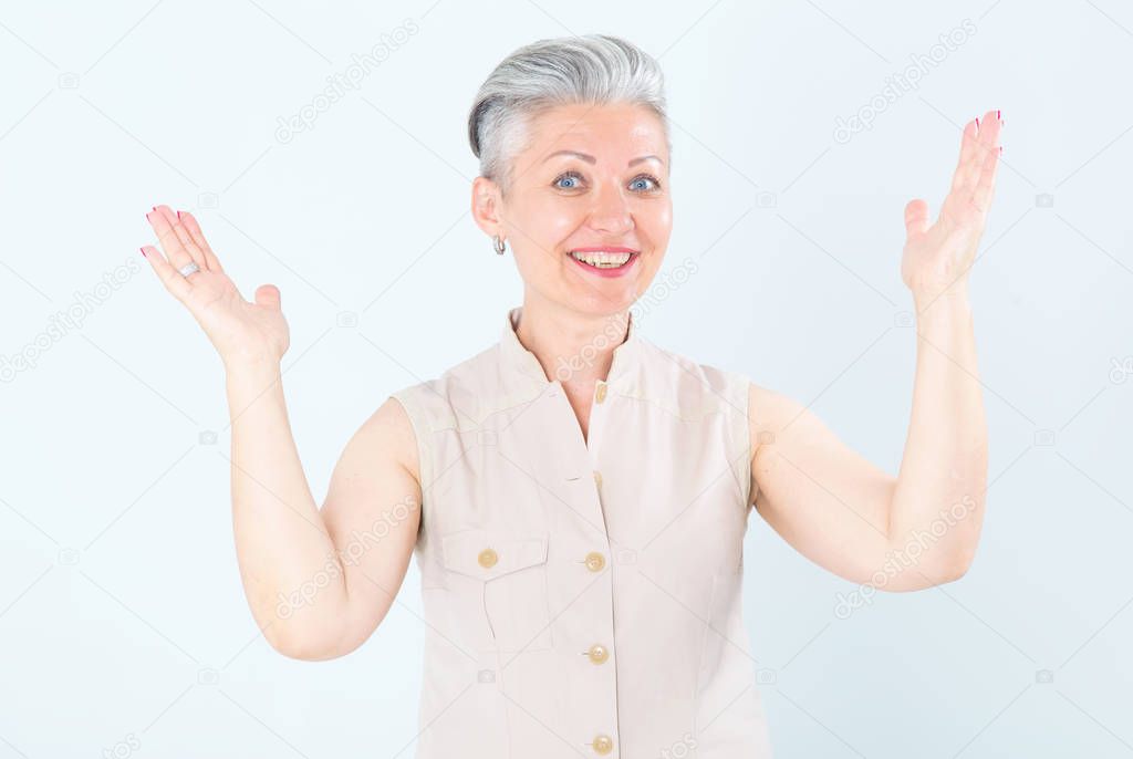Middle aged beautiful woman raised her hands up in delight, standing on a light white background.