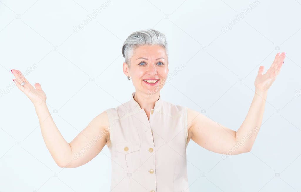 Mature woman raised her hands up in delight or surprise, standing on a light white background.