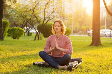 Güzel bir kadın doğa üzerine meditasyon yapmak için nilüfer pozisyonunda oturur. Yoga ve rahatlama. Gün batımında çalışma gününden sonra..
