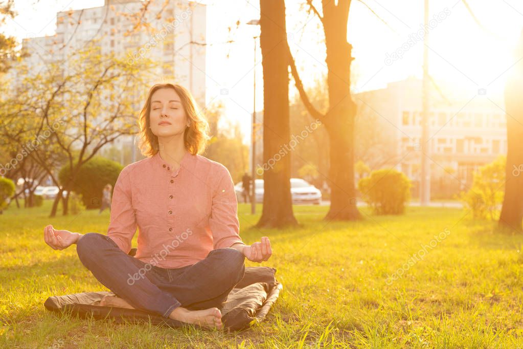 Beautiful woman sits in a lotus position for meditation on nature. Yoga and relaxation after a working day at sunset.