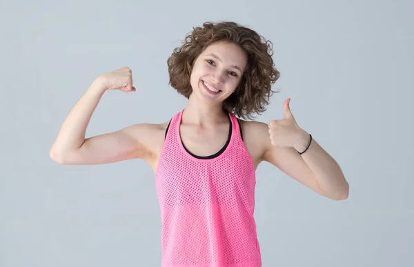 一个穿着粉色衣服参加健身班的快乐的年轻女子的画像 她站在浅薄的背景上 露出大拇指 手部肌肉 — 图库照片
