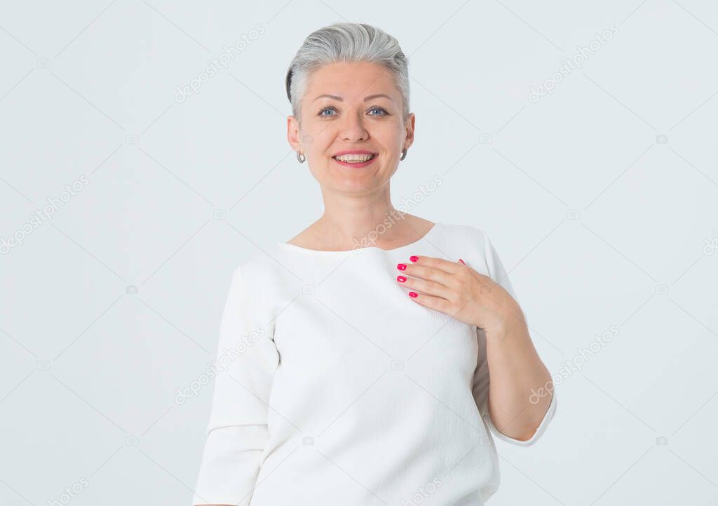 Portrait of a happy mature woman in a white dress standing on a light background.