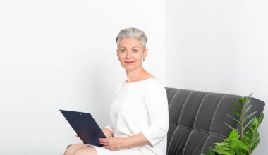 Ofisteki koltukta oturan olgun bir iş kadını. Başvuru formunu ya da sigorta belgelerini satış bürosundan doldurun.