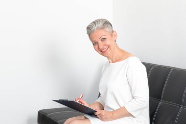 Ofisteki koltukta oturan olgun bir iş kadını. Başvuru formunu ya da sigorta belgelerini satış bürosundan doldurun.