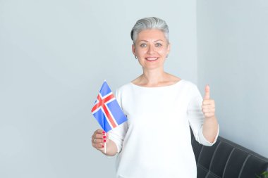 İzlanda bayrağı taşıyan orta yaşlı bir iş kadını, ofisin duvarında başparmağını gösteriyor..