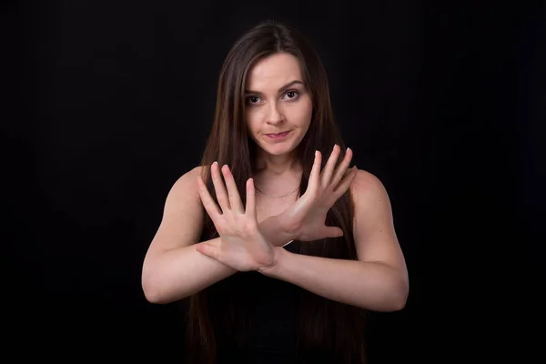 Denial and protest! Young woman is experiencing negative emotions, covering her with her hands, standing on a black background.