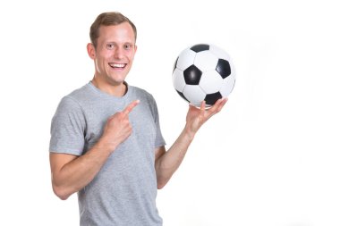 Futbol koçu. Genç adam elindeki bir futbol topunu işaret ediyor, beyaz bir arka planda izole edilmiş ve kameraya bakıyor..
