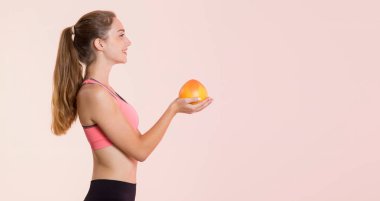 Genç bir kadın elinde limon ve portakal meyveleriyle gri bir arka planda durup kameraya bakıyor..