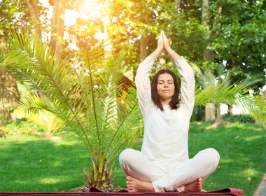 Yoga yapan kadın doğada dinleniyor. Lotuslu mutlu kadın kırmızı paspasın üzerinde oturuyor. Meditasyon kavramı.