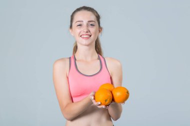 Elinde üç portakal meyvesi olan güzel genç bir kadın gri bir arka planda kameraya bakıyor..