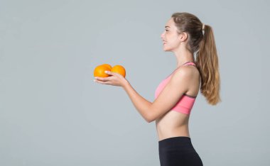 Gri arka planda turunçgil rengi portakalları olan güzel genç bir atletik kadın..