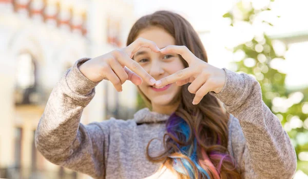 Teen girl, blurred face, holding hands in the shape of a heart in front of her face, gesture of support and health.