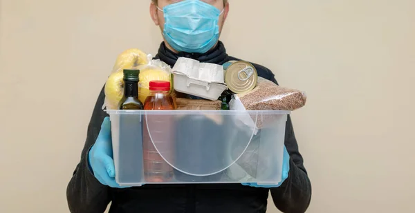 Man courier in protective medical mask and gloves deliver products in plastic box. Volunteer working in fund charity. Donation food during quarantine coronavirus.