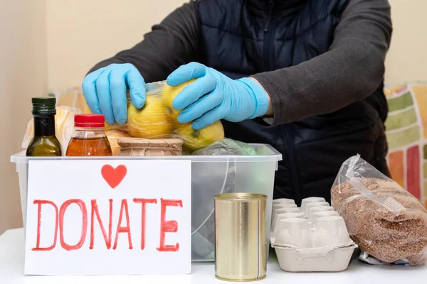 Volunteer man in protective medical  gloves work in fund charity food. Relief donate during quarantine coronavirus. Putting food in donation box.