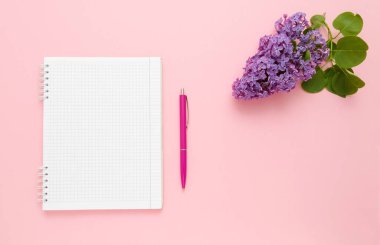 Üst görünüm boş sayfa not defteri, pembe arka planda kırmızı kalem ve mor leylak çiçekleri. Bir fikir metni için yer.