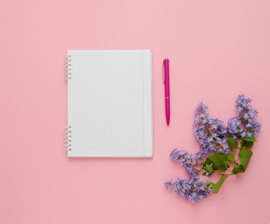 Pembe arka planda defter, kalem ve leylak çiçeğinin üst görünümü.