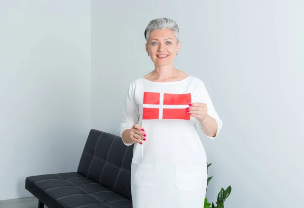 在办公室的背景下 拿着丹麦国旗的中年女商人正在看着摄像机 — 图库照片