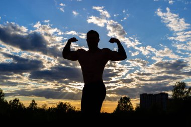 Günbatımı gökyüzünün arka planında güçlü kaslı bir adamın silueti. Akşamları sokakta spor..