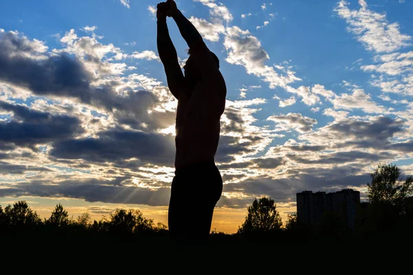 Silhouette male. Strong muscular man on a background of sunset sky. Fitness on the city park.