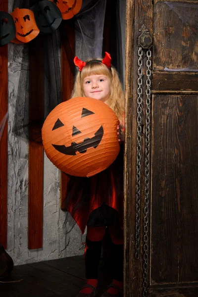 金色的万圣节魔鬼女孩与红色的角和微笑的南瓜在老木门室内 — 图库照片