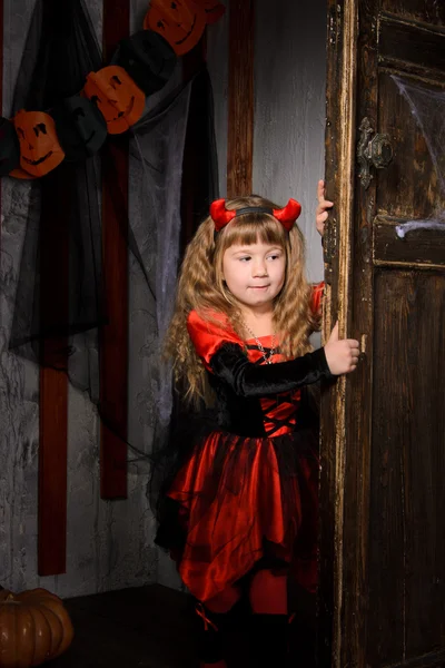 万圣节恶魔女孩在服装红色和黑色的角打开旧木门室内 — 图库照片