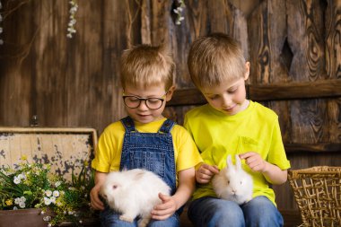 İki kardeş verandada oturup beyaz tavşanlarla oynayarak eğleniyorlar.