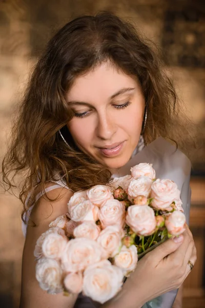 ピンクのバラの花束を手にした美しい巻き毛の女性の肖像 — ストック写真