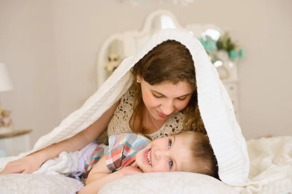 妈妈温和地看着她的儿子 他们躺在床上 床罩在明亮的卧室里 她小心地抱着孩子 — 图库照片