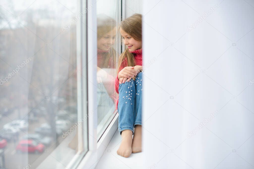 girl sits on windowsill, near windowpane, she wants to walk on street, but in  world there is coronavirus pandemic, and she remains at home in quarantine